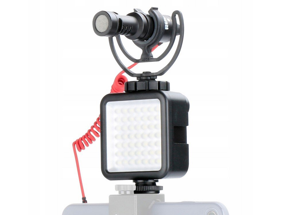 Na obrazie widoczna jest kompaktowa lampa LED w kolorze czarnym z siatką diod na przedniej części. Nad lampą zamontowany jest mikrofon z czerwonym kablem spiralnym.