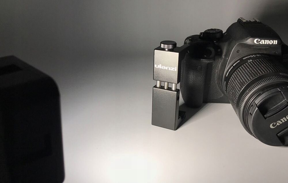 Na zdjęciu znajduje się aparat fotograficzny z obiektywem, obok którego stoi kompaktowa lampa LED z napisem \'ulanzi\'.