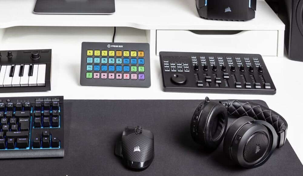 Na biurku znajduje się panel z wieloma kolorowymi przyciskami oznaczony napisem \'STREAM DECK\', obok klawiatura, myszka i słuchawki. W tle widoczne są inne urządzenia elektroniczne, w tym klawiatura MIDI i kontroler audio.