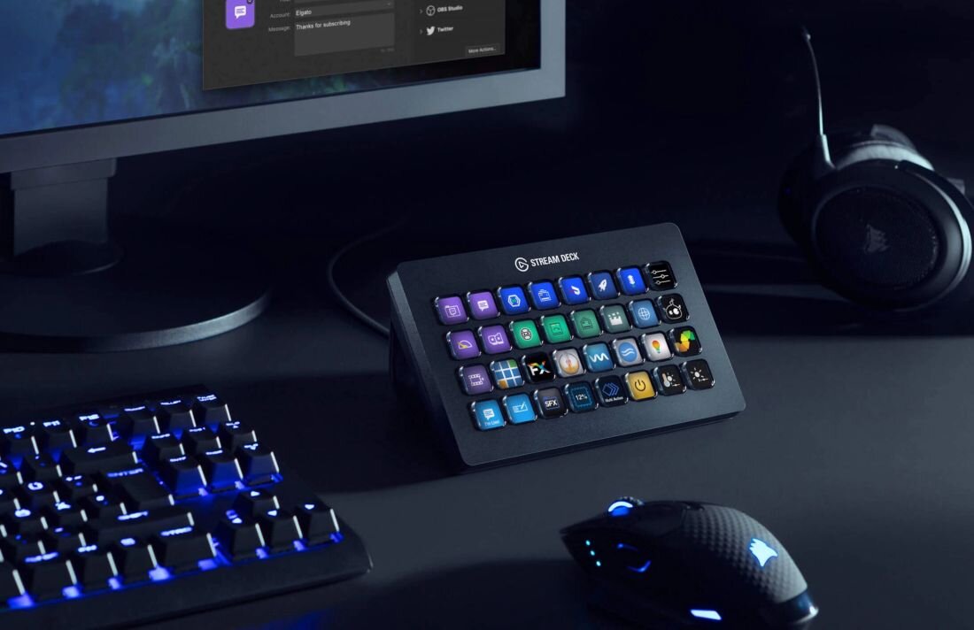 Na biurku znajduje się panel z wieloma kolorowymi przyciskami, obok klawiatury i myszy. Na panelu widoczny jest napis \'STREAM DECK\'.