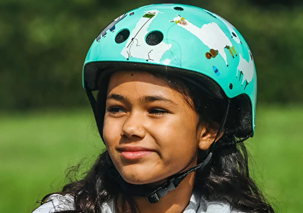 Kask HORNIT Lama Błękitny dla Dzieci (rozmiar S) trawnik dziecko w kasku patrzy w bok bezpieczeństwo wygoda aktywność