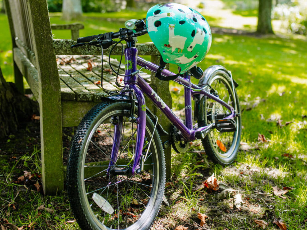 Kask HORNIT Lama Błękitny dla Dzieci (rozmiar S) park drzewa kask wisi na kierownicy roweru ochrona głowy dziecka bezpieczeństwo w sytuacjach niespodziewanych lekka budowa ciekawy wzór wygodne wnętrze komfort i spokój rodziców