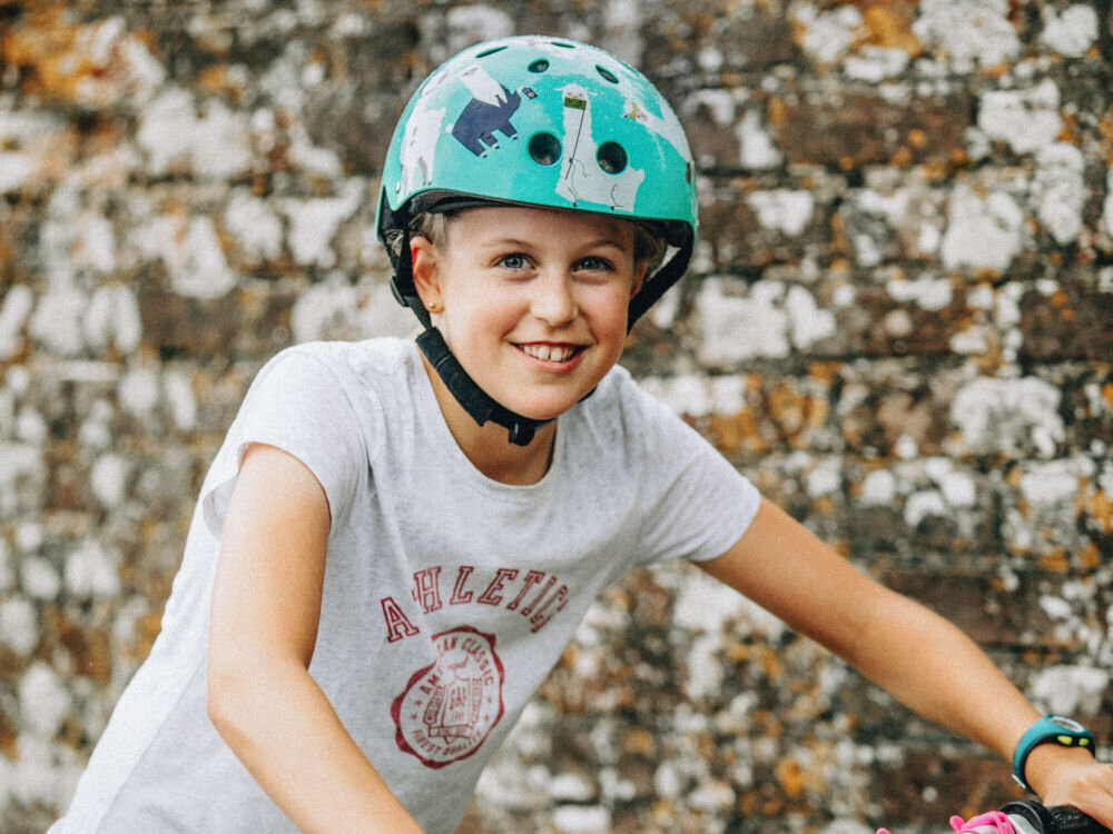 Kask HORNIT Lama Błękitny dla Dzieci (rozmiar S) dziecko w kasku na tle muru poliwęglanowa skorupa pianka EPS trwałość konstrukcji radzi sobie z pochłanianiem wstrząsów waga około 340 g wysoki komfort użytkowania