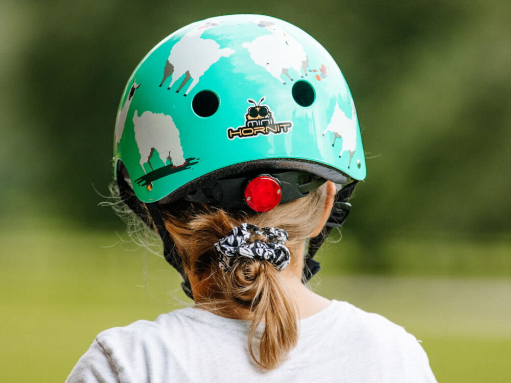 Kask HORNIT Lama Błękitny dla Dzieci (rozmiar S) dziecko w kasku widoczne od tyłu w tle rozmyta trawa specjalne miejsce na kucyk komfort noszenia kasku przez dzieci z dłuższymi włosami fryzura nie przeszkadza w jeździe kask stabilniej trzyma się głowy