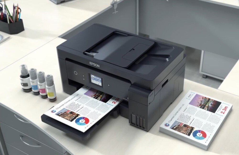Urządzenie wielofunkcyjne EPSON EcoTank L14150 urządzenie stojące na biurku z wydrukami wychodzącymi z niej, butelki z tuszem stojące obok drukowanie szybkość rozdzielczość druk dwustronny