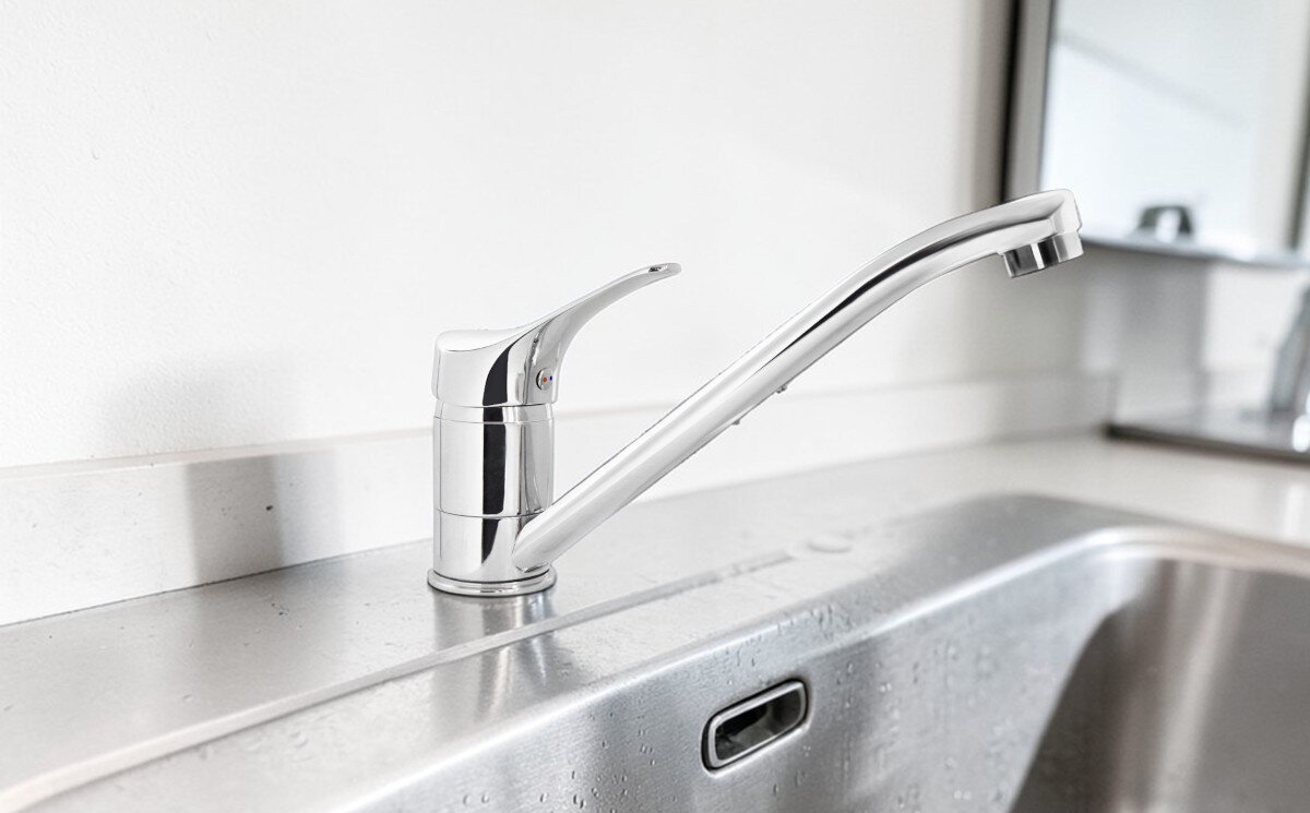 BATERIA KUCHENNA DEANTE NEO JOKO BOJ 060M CHROM Pierwsze zdjęcie przedstawia chromowaną baterię kuchenną zamontowaną na metalowym zlewie, z długą, prostą wylewką skierowaną w stronę komory. Powierzchnia zlewu jest lekko mokra, a tło stanowi jasna ściana i fragment lustra