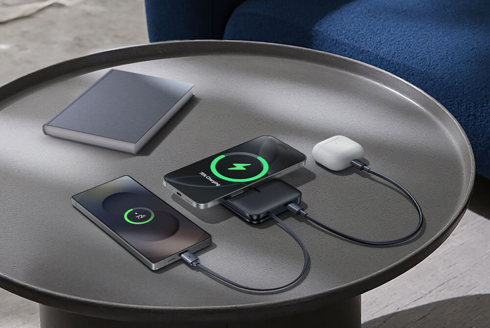 Powerbank BASEUS PicoGo AM61 QI2.2 10000 mAh 45W Czarny Na okrągłym stoliku leżą dwa smartfony i bezprzewodowe słuchawki AirPods, wszystkie ładowane za pomocą przewodów połączonych z powerbankiem Baseus. Obok znajduje się zamknięta książka.

