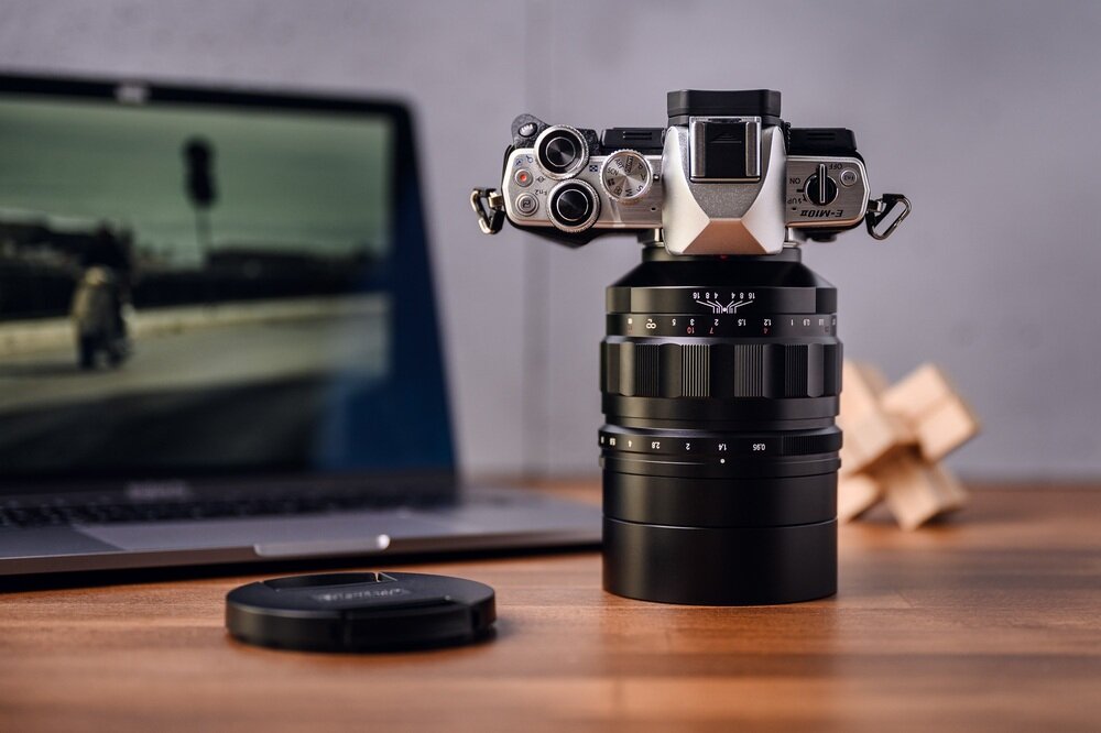 Obiektyw VOIGTLANDER 60 mm f-0.95 Nokton  Aparat Micro 4/3 z obiektywem Voigtländer Nokton 60 mm f/0,95 ustawiony na biurku, z widocznymi szczegółami konstrukcji i laptopem w tle, podkreślające precyzję i nowoczesny design obiektywu ogniskowa jasność f/0,95
