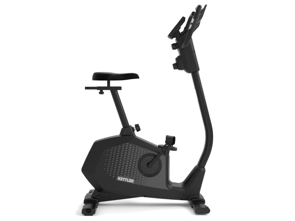 Osoba ćwiczy na rowerze magnetycznym KETTLER Ride 100 w jasnym, nowoczesnym wnętrzu z dużymi oknami. Na rowerze widoczne jest logo \'KETTLER\'.