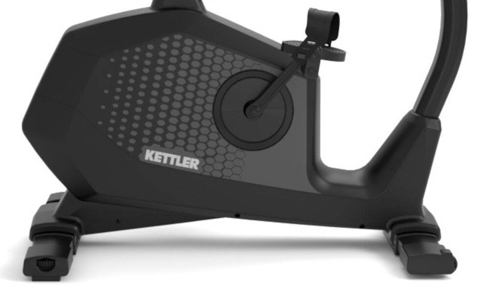 Osoba ćwiczy na rowerze magnetycznym z widocznym logo \'KETTLER\'. Rower stoi na drewnianej podłodze w jasnym pomieszczeniu.