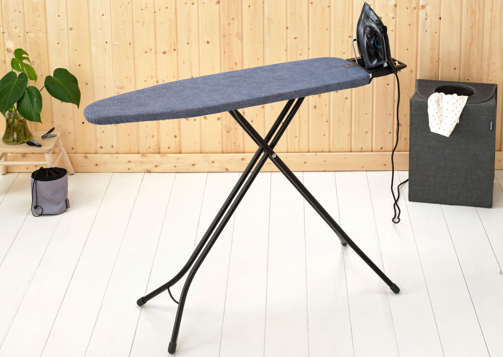 Deska do prasowania BRABANTIA 134203 Denim Blue 110 x 30 cm deska stoi bokiem ciemny pokrowiec czarne nóżki na podstawce stoi żelazko solidna budowa z trwałej, stalowej ramy o średnicy 22 mm wytrzymałość stabilność cztery solidne nogi mocne wsparcie konstrukcja odporna na codzienne intensywne użytkowanie staranna konstrukcja pełne bezpieczeństwo komfort podczas prasowania   