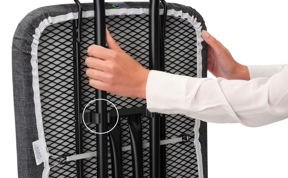 Deska do prasowania BRABANTIA 134746 Denim Black 124 x 45 cm osoba trzyma złożoną deskę metalowe czarne elementy białe tło wygodne przechowywanie i transport blokada transportowa bezpieczne złożenie blokada dziecięca zapobieganie przypadkowemu otwarciu dodatkowe bezpieczeństwo w domu łatwa do przechowywania małe przestrzenie 