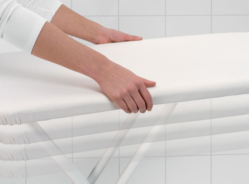 Deska do prasowania BRABANTIA 134708 Spring Bubbles 124 x 45 cm osoba trzyma deskę podnosi ją w górę jasny pokrowiec jasne tło płynna regulacja wysokości od 75-98 cm maksymalny komfort użytkowania dostosowanie wysokości ergonomiczny optymalna pozycja pracy wygoda redukcja zmęczenia 