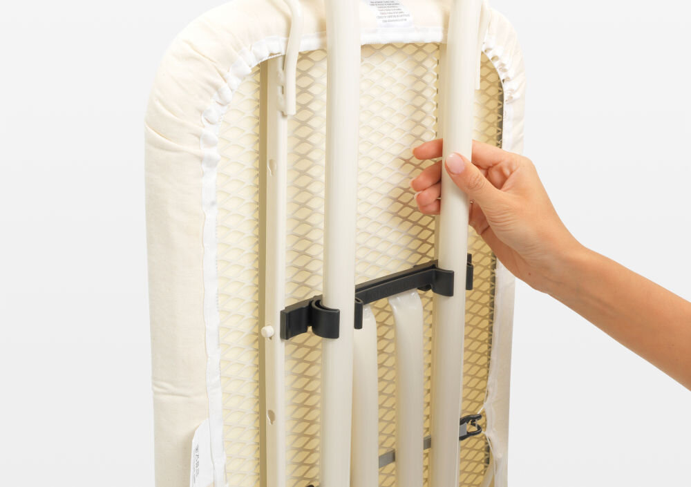 Deska do prasowania BRABANTIA 134708 Spring Bubbles 124 x 45 cm osoba trzyma złożoną deskę białe metalowe elementy białe tło  wygodne przechowywanie i transport blokada transportowa bezpieczne złożenie blokada dziecięca zapobieganie przypadkowemu otwarciu dodatkowe bezpieczeństwo w domu łatwa do przechowywania małe przestrzenie 