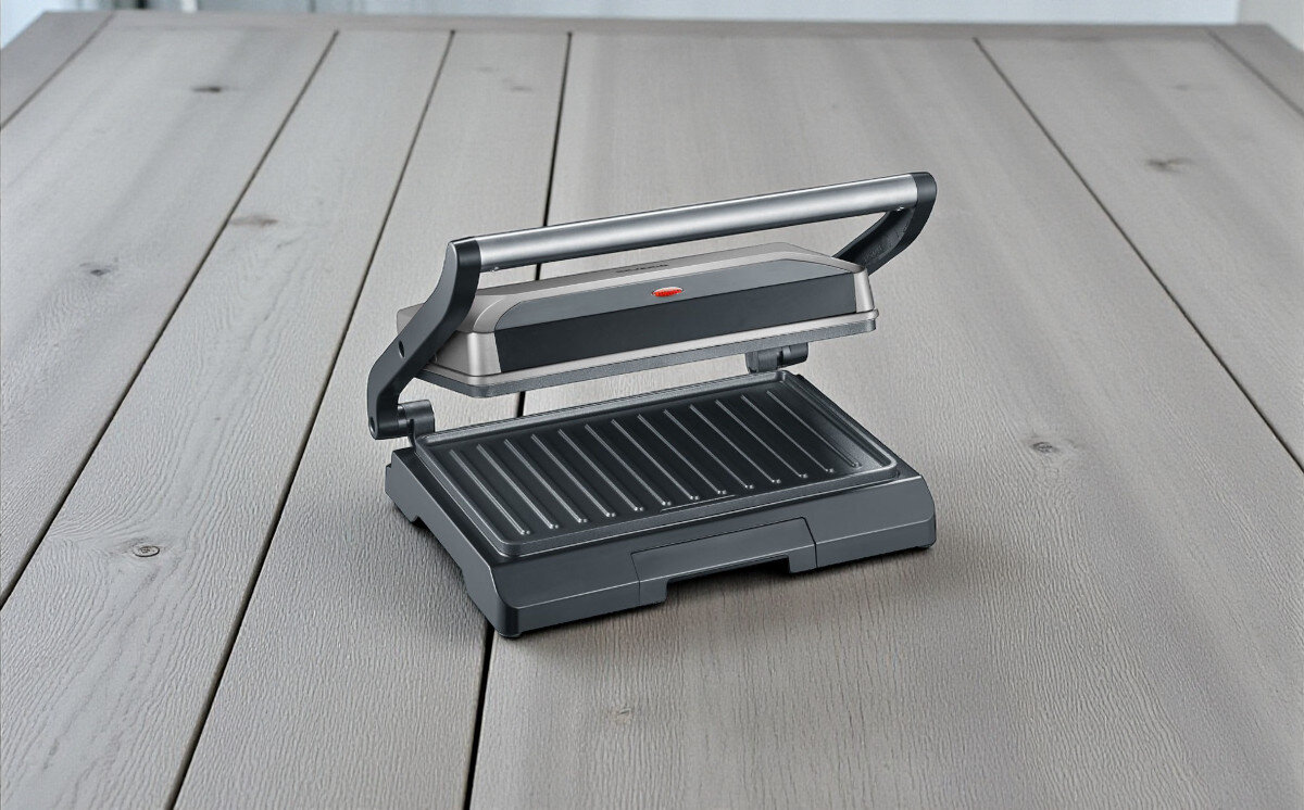Grill elektryczny SEVERIN KG 2394, przywieranie, czyszczenie, jednocześnie, posiłek, na drewnianym blacie stoi gtill frontem lewo skos