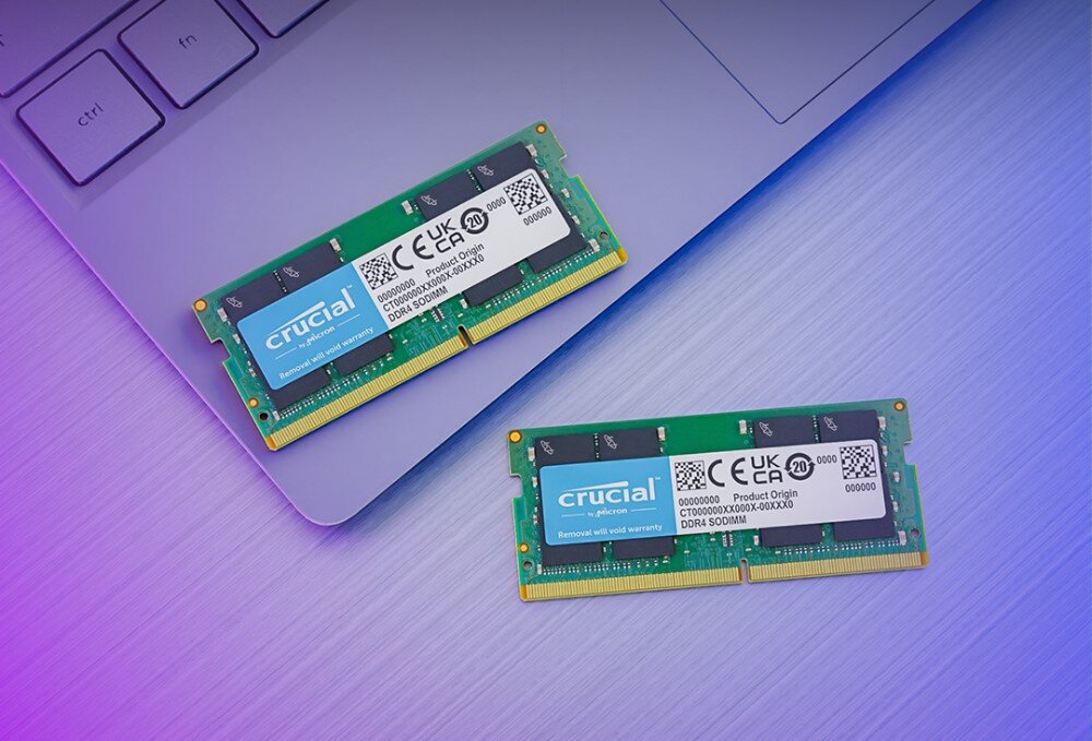 Pamięć RAM CRUCIAL Dwa zielone moduły pamięci leżące obok laptopa na fioletowo-niebieskiej powierzchni, z widocznymi etykietami technicznymi, parametry, przeznaczenie