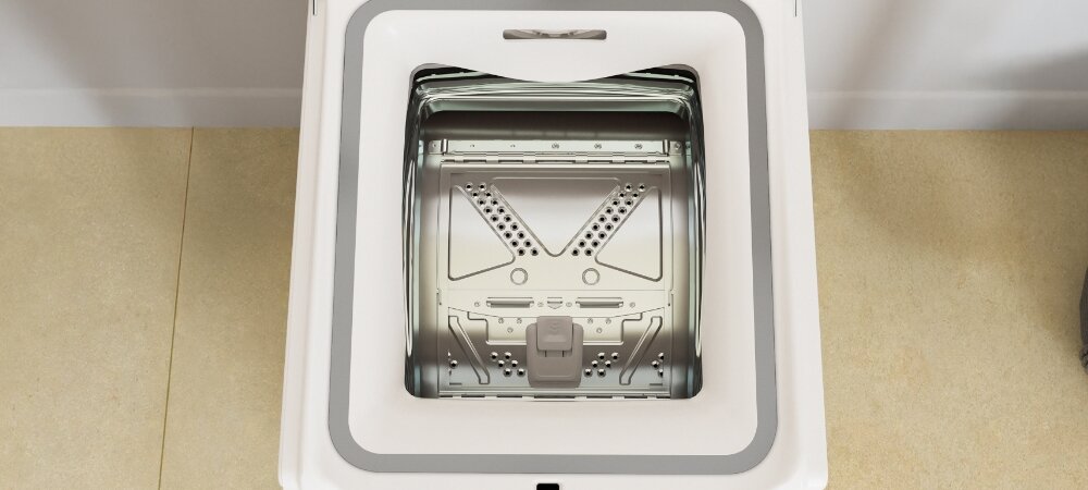 Widok z góry na otwartą pralkę z widocznym bębnem i elementami metalowymi wewnątrz. Pralka jest w jasnym kolorze, a podłoga ma beżowy odcień.