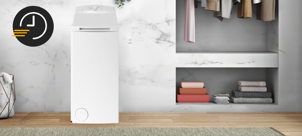 Biała pralka ładowana od góry stoi w pomieszczeniu z marmurowymi ścianami i drewnianą podłogą. Obok pralki znajduje się wnęka z półkami, na których leżą złożone ubrania i książki.