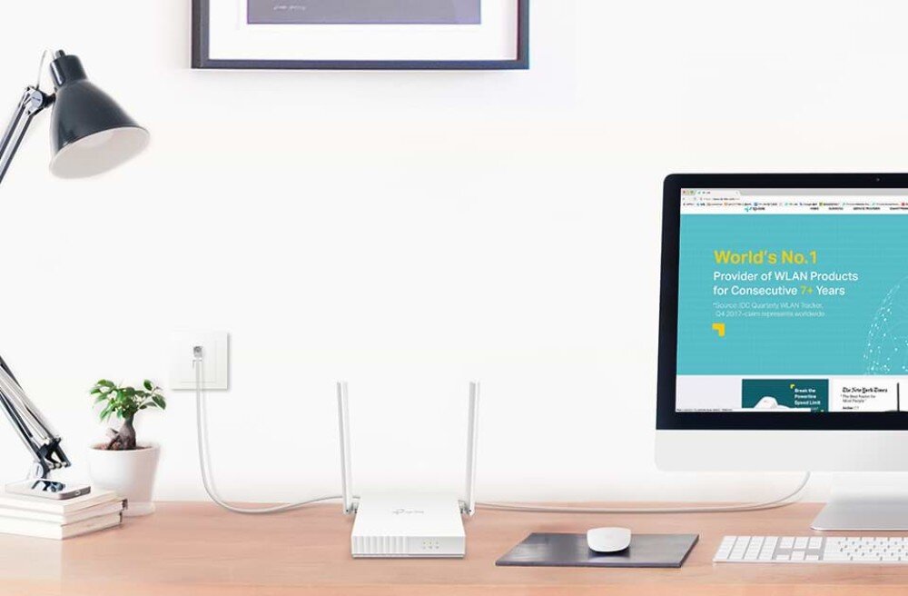 Router TP-LINK TL-WR820N Router ustawiony na drewnianym biurku obok monitora, klawiatury i dekoracyjnej buteleczki z patyczkami zapachowymi, tryby działania