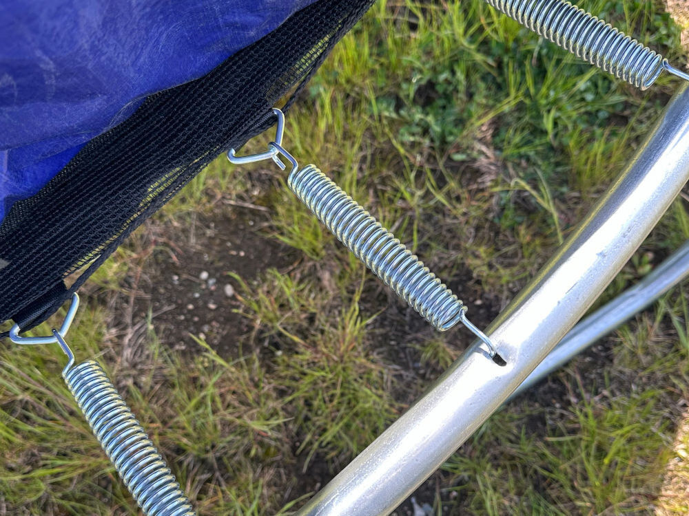 Trampolina ENERO FI 244 cm, wymiary, naciąg, długość, sprężyny,Zbliżenie na konstrukcję trampoliny wraz ze sprężynami oraz osłonami