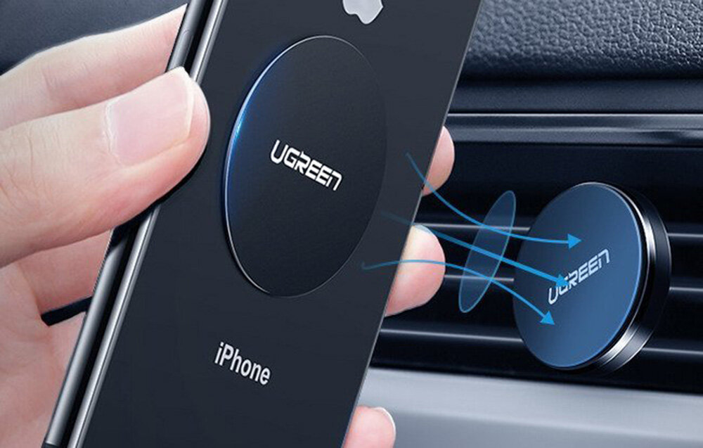 Osoba trzyma telefon z zamocowaną metalową płytką z logo \'UGREEN\', zbliżając go do magnetycznego uchwytu w samochodzie. Na telefonie widoczny jest napis \'iPhone\'.