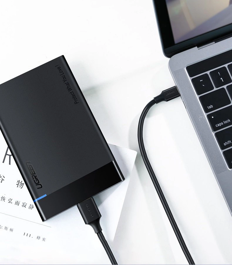 Na obrazie widać czarny dysk zewnętrzny z logo \'UGREEN\' podłączony do laptopa za pomocą czarnego kabla USB. Na dysku widoczny jest napis \'Protect What You Love\'.