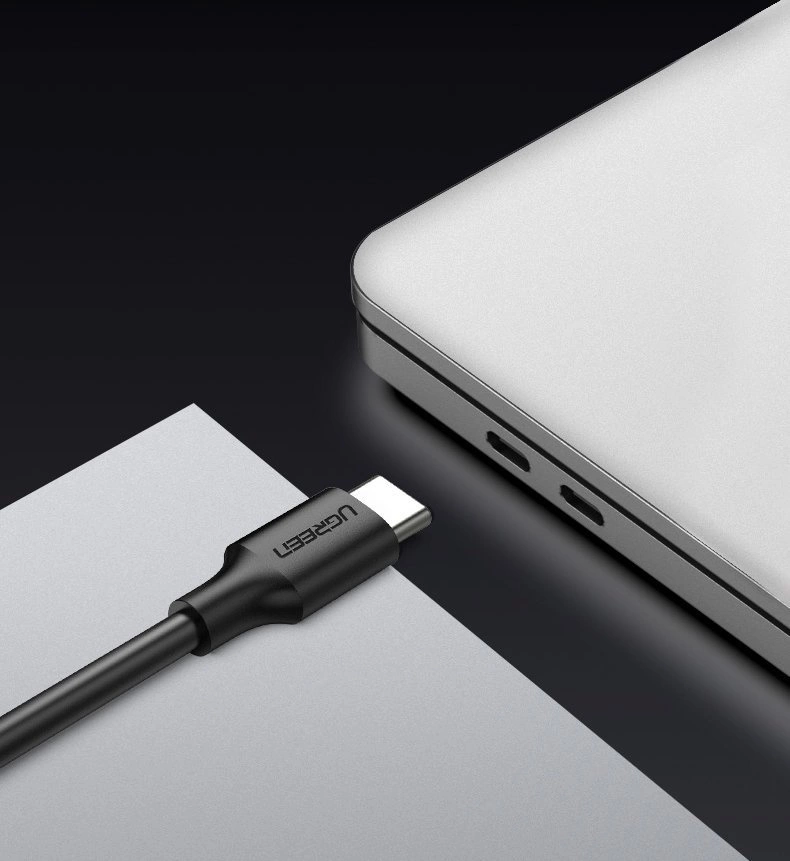 Na obrazie widoczny jest czarny kabel USB z logo \'UGREEN\' obok srebrnego laptopa z dwoma portami USB-C.