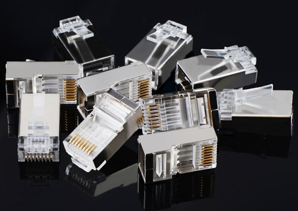 Wtyk UGREEN 20333 Kilkanaście metalowych wtyków RJ45 rozrzuconych na czarnym, błyszczącym podłożu, w którym widać ich odbicia