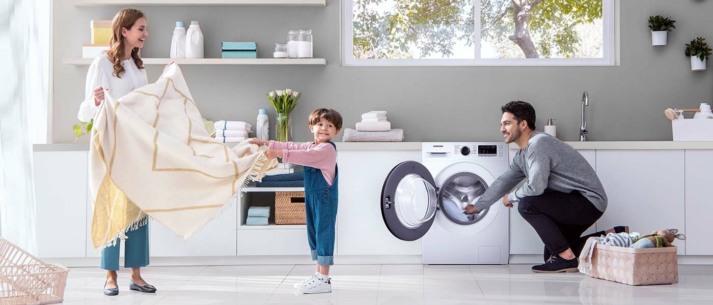 Uśmiechnięta kobieta, mężczyzna i dziecko wyciągają pranie z pralki