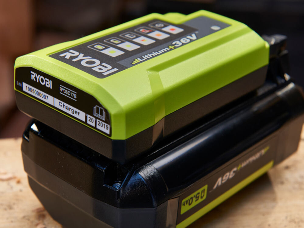 Ładowarka RYOBI RY36C17A 36V 1.7A, ładowanie, energia, 1.7A, akumulator, Zbliżenie na ładowarkę podpiętą do akumulatora na blacie warsztatowym