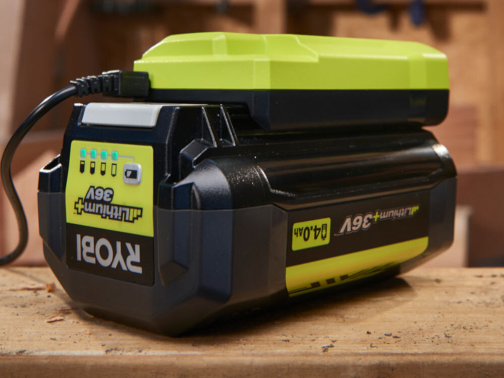 Ładowarka RYOBI RY36C17A 36V 1.7A, seria, model, współpraca, 36V, Na zdjęciu akumulator i ładowarka podpięta pod sieć zasilającą, wszystko na blacie w warsztacie