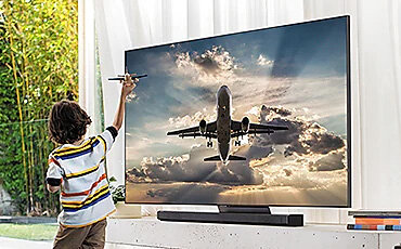 Telewizor wyświetla obraz samolotu. Dziecko przed ekranem bawi się małym samolotem. Q95TDTXXH