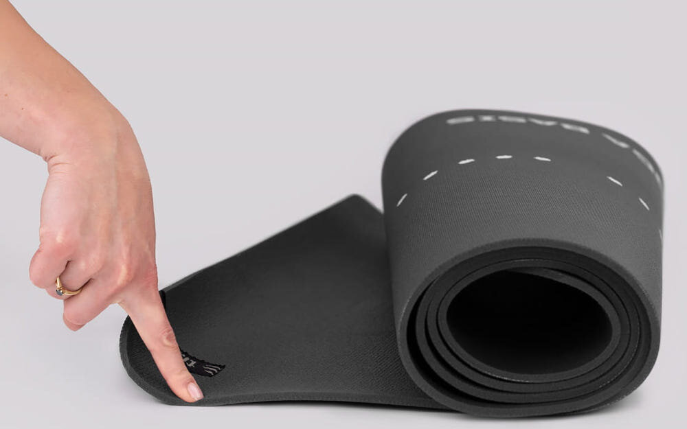 Mata do jogi TIGUAR Yoga Basis Grafitowy jasne tło zwinięta mata osoba trzyma jednym palcem jeden koniec maty widok z boku regularne przecieranie maty wilgotną ściereczką z wodą lub delikatnym środkiem czyszczącym poprawia przyczepność powierzchni każdy kolejny trening odbywa się w bardziej higienicznych warunkach