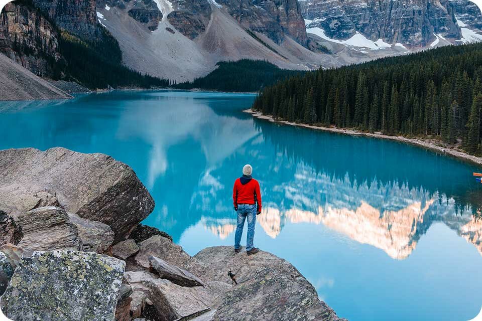 Stojący mężczyzna na skale w górach, przed nim jezioro Stojący mężczyzna na skale w górach, przed nim jezioro