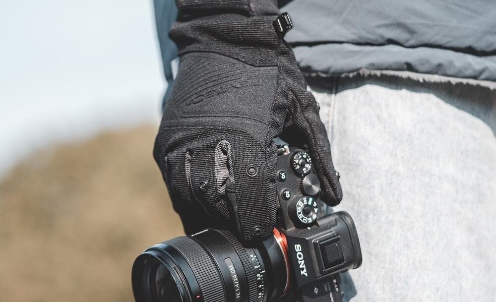 Osoba trzyma aparat fotograficzny w rękawiczkach. Na aparacie widoczne jest logo \'SONY\'.