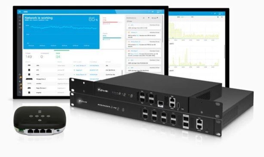 Router UBIQUITI UF-WIFI Ufiber Małe urządzenie abonenckie stojące obok dwóch szerokich jednostek centralnych typu rack na tle monitorów z wyświetlonymi niebieskimi wykresami wydajności sieci
