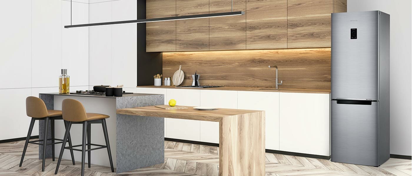Biało drewniana kuchnia z wyspą i dwoma krzesłami barowymi oraz lodówką Samsung w kolorze szczotkowanej stali nierdzewnej