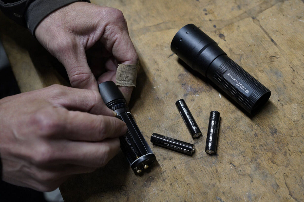 Latarka LEDLENSER P7 Core, zasilanie, trzy, tryby, lumeny, zasięg, osoba obsługuje rękoma rozebraną latarkę i baterie