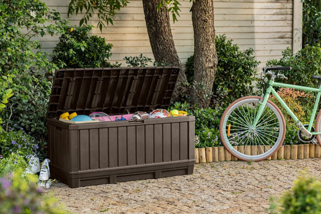 Skrzynia ogrodowa KETER Kentwood 249461 350L Brązowy, pojemność, wymiary, przestrzeń, organizacja, Otwarta skrzynia Kentwood wypełniona sprzętem sportowym obok roweru.