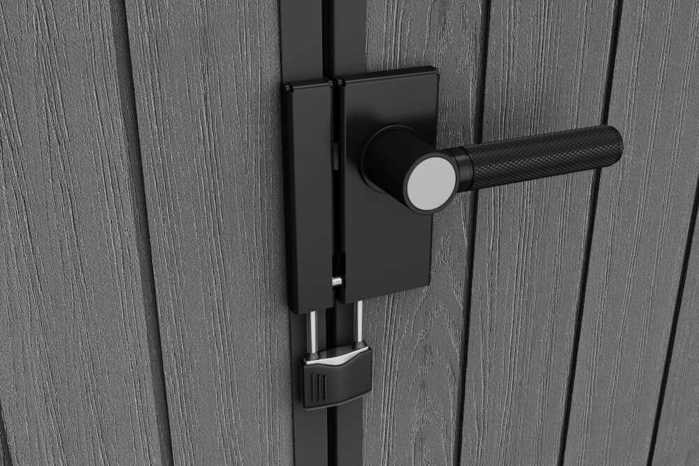 Zbliżenie na czarną klamkę i zamek na szarych drzwiach z teksturą drewna. Widoczna jest także kłódka zabezpieczająca zamek.