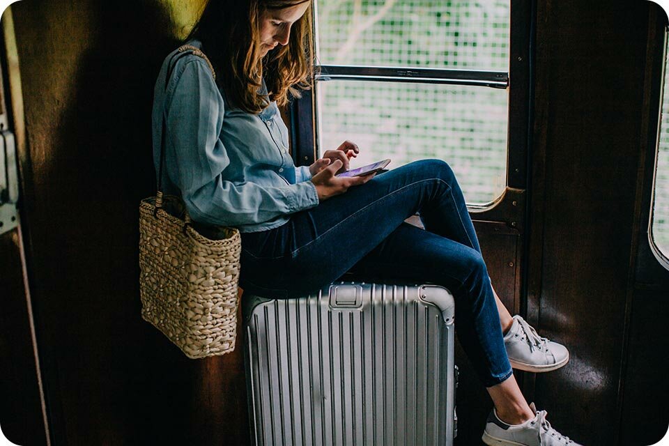 Kobieta siedząca na walizce podczas podróży używa telefonu Kobieta siedząca na walizce podczas podróży używa telefonu