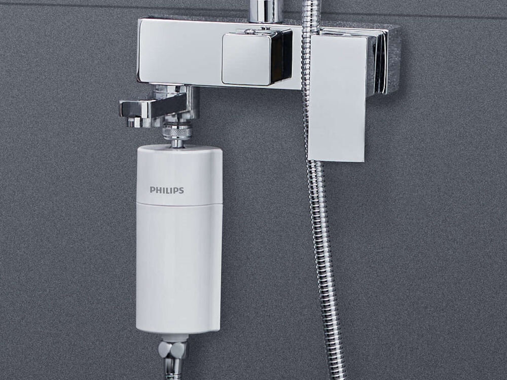 Biały filtr prysznicowy z napisem \'PHILIPS\' zamontowany na chromowanej armaturze prysznicowej. Obok widoczny jest metalowy wąż prysznicowy.