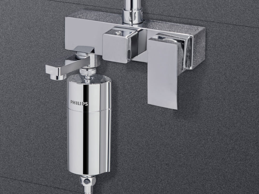 Srebrny filtr prysznicowy z logo PHILIPS zamontowany na ścianie z ciemnego materiału. Filtr ma cylindryczny kształt i jest częścią systemu prysznicowego.