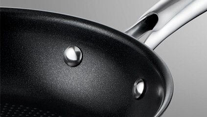 Zbliżenie na wnętrze patelni z czarną, nieprzywierającą powłoką i metalowym uchwytem przymocowanym za pomocą nitów.