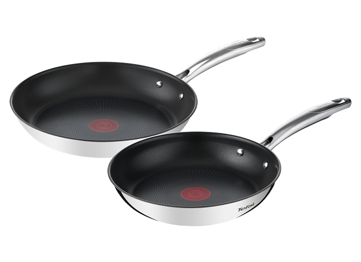 Na obrazie widoczne są dwie patelnie z czarnym wnętrzem i srebrnymi uchwytami. Na dnie każdej patelni znajduje się czerwony okrągły wzór.