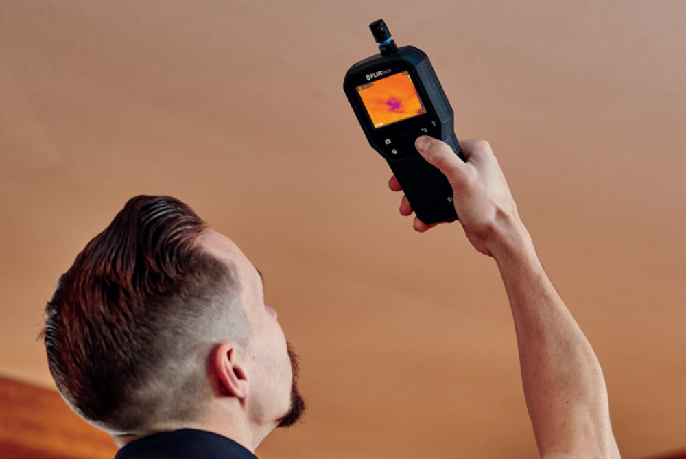 FLIR MR277 budownictwie, konserwacji obiektów i diagnostyce technicznej kontroli systemów HVAC analizie miejsc o podwyższonej temperaturze - męzczyzna z kamerą w ręku na tle sufitu