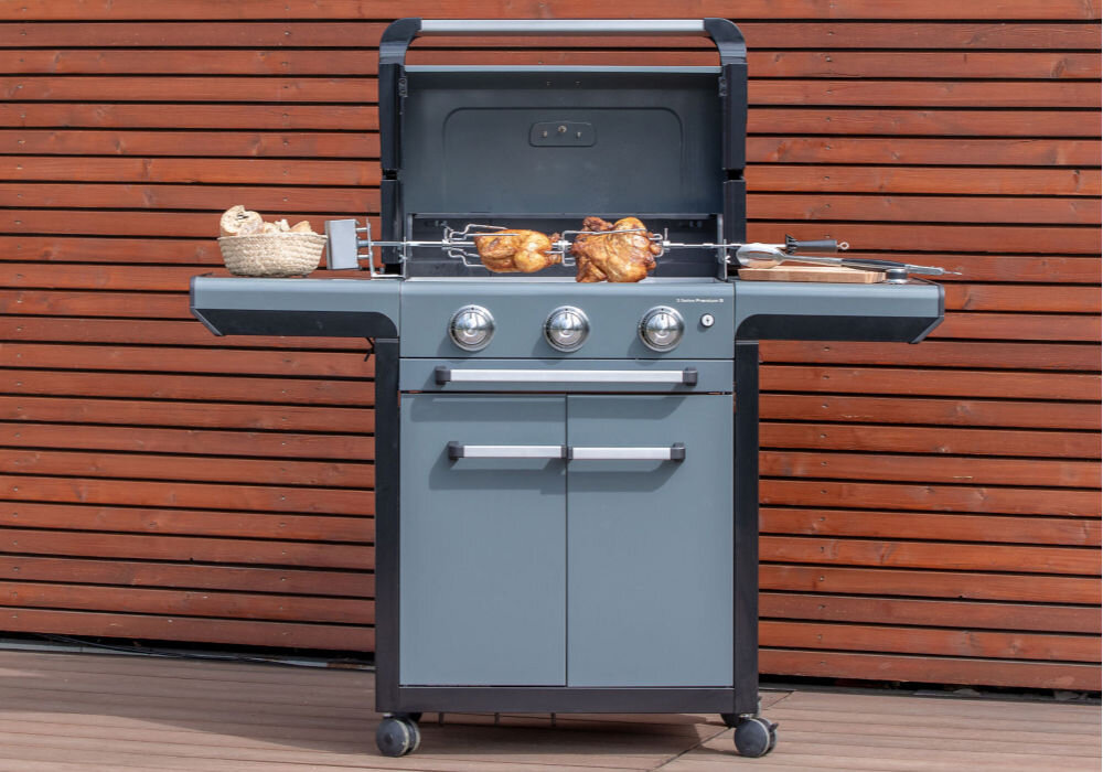 Rożen elektryczny CAMPINGAZ Culinary Modular 2000036962, rożen, gotowanie, smażenie, komfort, grill stoi frontem na wprost w tle drewniana ściana w tle ogród