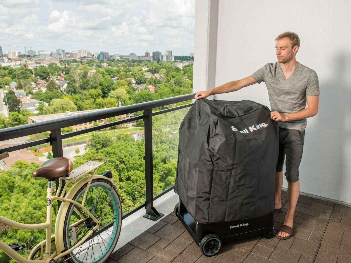 Pokrowiec na grilla BROIL KING BK GEM 67420, grill, ochrona, ogród, schowanie, mężczyzna trzyma pokrowiec na grilla na balkonie