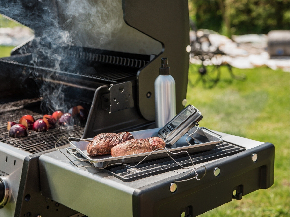 Rozpylacz oleju BROIL KING Grill Pro 50945, mgiełka, olej, potrawy, grillowanie, Taca z upieczonym mięsem i termometrem grillowym leży na półce grilla gazowego, obok stoi metalowa butelka ze spryskiwaczem, w tle warzywa grillujące się na ruszcie.