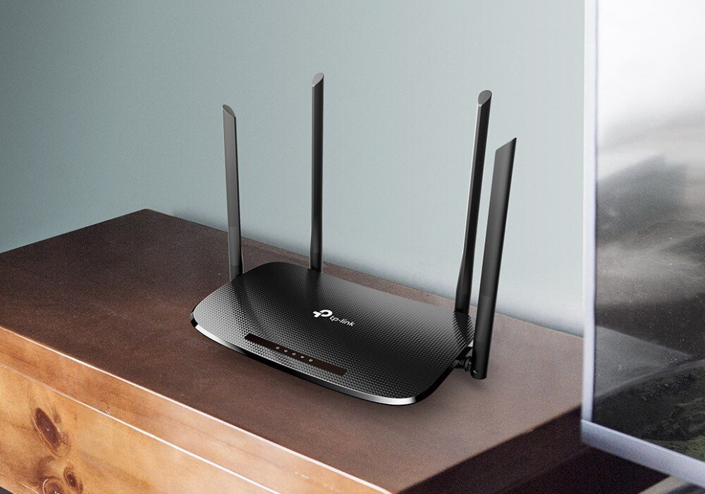 Router TP-LINK Archer VR300 Router z czterema antenami umieszczony na drewnianym meblu przy ścianie. Obok częściowo widoczny ekran telewizora, opis